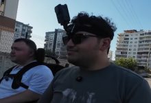 Kent ortamında yan yana iki akülü sandalyeyle Furkan Ulusoy ve Batuhan Fidan seyahat ediyor, Furkan Ulusoy ise başına taktığı aksiyon kamerasıyla görüntü kaydı alıyor.