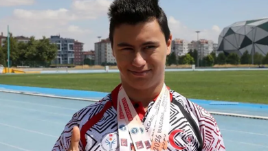 Görselde milli sporcu, atletizm pistinde boynundaki madalyalarıyla poz vererek başparmağını kaldırıyor.