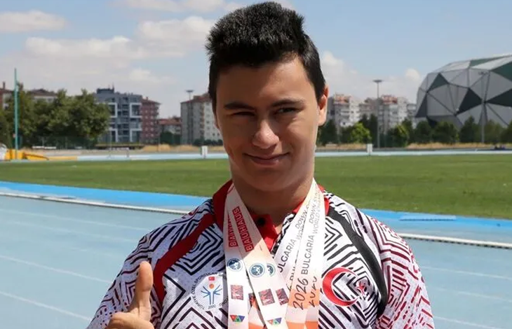 Görselde milli sporcu, atletizm pistinde boynundaki madalyalarıyla poz vererek başparmağını kaldırıyor.