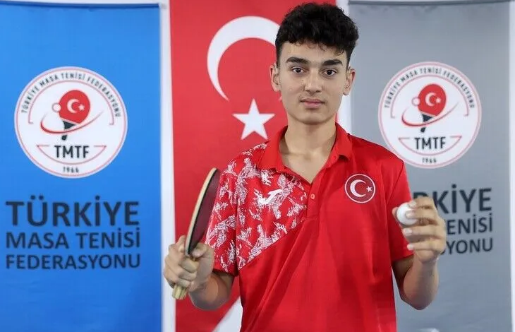 Görselde, Ebubekir İnce kırmızı Türkiye formasıyla elinde masa tenisi raketi ve top tutarak kameraya bakıyor. Arka planda Türk bayrağı ile Türkiye Masa Tenisi Federasyonu logolarının bulunduğu panolar yer alıyor.