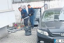Otomobil paspası yıkayan bir personel ve yanında bulunan başka bir erkek kendisini izliyor.