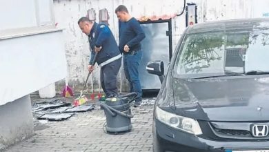Otomobil paspası yıkayan bir personel ve yanında bulunan başka bir erkek kendisini izliyor.