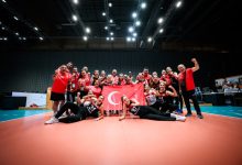 Oturarak Voleybol Kadın Milli Takımı ve teknik heyet, Türk bayrağı tutarak poz veriyor.