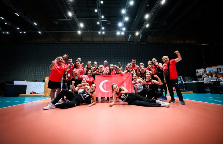 Oturarak Voleybol Kadın Milli Takımı ve teknik heyet, Türk bayrağı tutarak poz veriyor.