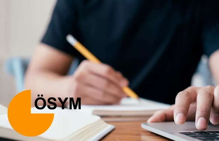 Görselin üst bölümünde, ahşap bir çalışma masasında ders çalışan veya sınav hazırlığı yapan siyah tişörtlü bir adayın elleri ve çalışma alanı yakın plandan görülüyor. Sol eliyle sarı bir kurşun kalemi tutarak deftere yazı yazan adayın sağ eli ise gri renkli dizüstü bilgisayarın klavyesinin üzerinde duruyor. Görselin sol alt köşesinde ÖSYM'nin turuncu renkli stilize amblemi ve siyah büyük harflerle "ÖSYM" yazısı yer alıyor.
