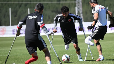 Görselin üst bölümünde, güneşli bir günde yeşil çim sahada kanedyenleriyle (koltuk değnekleri) antrenman yapan üç ampute milli futbolcu görülüyor. Sırtında beyaz harflerle "TÜRKİYE" yazan siyah formalı futbolcu arkası dönük şekilde topa hamle yaparken; ortadaki kıvırcık saçlı, siyah antrenman formalı oyuncu yerdeki futbol topuna odaklanarak kanedyenlerinden destek alıp hücuma kalkıyor. Sağ tarafta ise beyaz formalı diğer oyuncu tek bacağı üzerinde dengesini sağlayarak pozisyonu takip ediyor; arka planda açık renkli antrenman panoları ve ağaçlık alan seçiliyor.