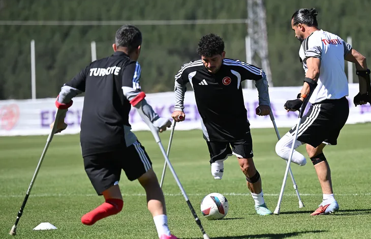Görselin üst bölümünde, güneşli bir günde yeşil çim sahada kanedyenleriyle (koltuk değnekleri) antrenman yapan üç ampute milli futbolcu görülüyor. Sırtında beyaz harflerle "TÜRKİYE" yazan siyah formalı futbolcu arkası dönük şekilde topa hamle yaparken; ortadaki kıvırcık saçlı, siyah antrenman formalı oyuncu yerdeki futbol topuna odaklanarak kanedyenlerinden destek alıp hücuma kalkıyor. Sağ tarafta ise beyaz formalı diğer oyuncu tek bacağı üzerinde dengesini sağlayarak pozisyonu takip ediyor; arka planda açık renkli antrenman panoları ve ağaçlık alan seçiliyor.