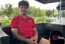 Görselin üst bölümünde, açık alandaki bir tesiste hasır koltukta oturarak röportaj veren milli ampute futbolcu Barış Telli yer alıyor. Kıvırcık koyu renk saçlı ve hafif sakallı olan Telli, göğsünde Türk bayrağı arması bulunan kırmızı milli takım polo tişörtü ve siyah şort giymiş halde tebessüm ederek kameraya bakıyor. Sağ alt köşede İhlas Haber Ajansı (İHA) logolu mikrofon ucu görülürken; arka planda ise yeşil ağaçlar, çimlik alan, yapay gölet/havuz ve modern tesis yapıları seçiliyor.