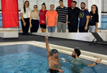 Alt alta yer alan 1. üstteki görsel: Kapalı bir havuz alanında, sekiz kişilik bir grup yan yana duruyor. Arkalarında kırmızı-beyaz dikey panolar ve havuz kenarı görülüyor. Grup, etkinlik veya eğitim ortamında bir araya gelmiş izlenimi veriyor. 2. alttaki görsel: Havuz içinde iki kişi bulunuyor. Bone takan kişi kolunu yukarı kaldırmış; yanındaki kişi ona destek veriyor veya yüzme eğitimi veriyor gibi görünüyor. Sahne, yüzme dersi ya da su terapisi uygulamasını yansıtıyor.