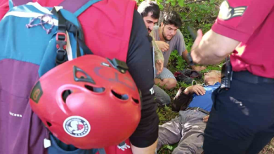 Görselde, çalılık ve otluk bir alanda yerde yatan yaşlı bir kişiye yardım eden sivil kıyafetli iki erkek ve iki resmi görevli görülmektedir. Ön plandaki görevlinin sırt çantasına takılı kırmızı bir kask ve yanında "Quechua" yazılı mor bir çanta yer almaktadır; arkadaki resmi görevlinin ise omzunda rütbe işareti bulunan kırmızı bir gömlek ve belinde telsiz taşıdığı fark edilmektedir.