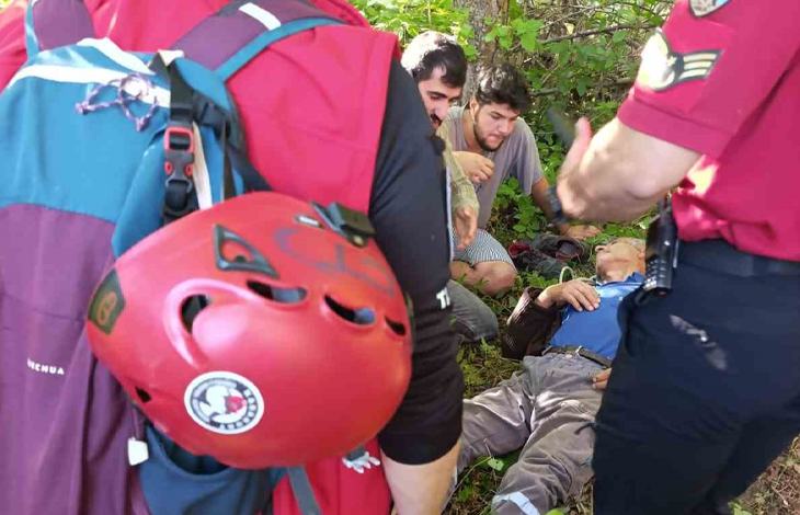 Görselde, çalılık ve otluk bir alanda yerde yatan yaşlı bir kişiye yardım eden sivil kıyafetli iki erkek ve iki resmi görevli görülmektedir. Ön plandaki görevlinin sırt çantasına takılı kırmızı bir kask ve yanında "Quechua" yazılı mor bir çanta yer almaktadır; arkadaki resmi görevlinin ise omzunda rütbe işareti bulunan kırmızı bir gömlek ve belinde telsiz taşıdığı fark edilmektedir.