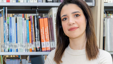 Çocuk ve ergenlerle çalışan Klinik Psikolog Eliz Avcı, sakin ve güven veren bir duruşa sahip. Omuz hizasında düz, açık renk saçları var; açık tonlarda, sade bir üst giymiş. Arkasında farklı renk ve boyutlarda kitaplarla dolu bir raf bulunuyor. Ortam, akademik bir çalışma alanı hissi veriyor. Genel görünümü, profesyonel, dikkatli ve danışanlarına karşı sıcak bir yaklaşımı olan bir uzman izlenimi oluşturuyor.