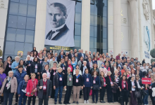 Görselin üst bölümünde, modern ve sütunlu büyük bir kültür veya kongre merkezinin merdivenlerinde toplanmış çok kalabalık bir katılımcı grubu yer alıyor. Merdivenleri dolduran kadınlı erkekli kalabalığın boyunlarında etkinlik tanıtım kartları (akreditasyon kartları) asılıyken, sağ tarafta bir katılımcı üzerinde beyaz harflerle "DENİZLİ" yazan kırmızı küçük bir pankart tutuyor. Binanın cam cephesinde dev bir Mustafa Kemal Atatürk posteri asılı duruyor ve posterin hemen altındaki tabelada "Ferdi Zeyrek Millet Çarşısı" yazısı seçiliyor.