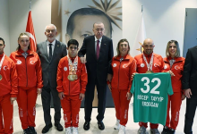 Görselin üst bölümünde, Cumhurbaşkanlığı Külliyesi'nde Cumhurbaşkanı Recep Tayyip Erdoğan ile Türkiye Özel Sporcular Spor Federasyonu temsilcileri ve milli sporcularının bir araya gelerek çektirdiği hatıra fotoğrafı yer alıyor. Ortada koyu renk takım elbiseli ve kırmızı kravatlı Cumhurbaşkanı Erdoğan dururken, iki yanında federasyon yetkilileri ile kırmızı milli takım eşofmanı giymiş, boyunlarında madalyaları asılı olan özel sporcular sıralanıyor. Sağ tarafta yer alan sporculardan biri, üzerinde beyaz harflerle "32 RECEP TAYYİP ERDOĞAN" yazılı yeşil renkli formayı açarak sergiliyor. Arka planda Türk bayrağı, Cumhurbaşkanlığı forsu ve duvarda büyük bir portre yer alıyor.