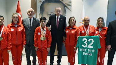 Görselin üst bölümünde, Cumhurbaşkanlığı Külliyesi'nde Cumhurbaşkanı Recep Tayyip Erdoğan ile Türkiye Özel Sporcular Spor Federasyonu temsilcileri ve milli sporcularının bir araya gelerek çektirdiği hatıra fotoğrafı yer alıyor. Ortada koyu renk takım elbiseli ve kırmızı kravatlı Cumhurbaşkanı Erdoğan dururken, iki yanında federasyon yetkilileri ile kırmızı milli takım eşofmanı giymiş, boyunlarında madalyaları asılı olan özel sporcular sıralanıyor. Sağ tarafta yer alan sporculardan biri, üzerinde beyaz harflerle "32 RECEP TAYYİP ERDOĞAN" yazılı yeşil renkli formayı açarak sergiliyor. Arka planda Türk bayrağı, Cumhurbaşkanlığı forsu ve duvarda büyük bir portre yer alıyor.