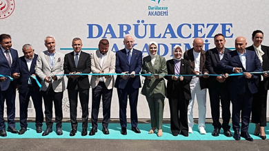 Görselin üst bölümünde, açık havada kurulan tören sahnesinde yan yana dizilmiş protokol heyeti, ellerindeki makaslarla açılış kurdelesini keserken yer alıyor. Arka plandaki beyaz fonda büyük harflerle "DARÜLACEZE AKADEMİ" yazısı, kurumun logosu ve sol üst köşede T.C. Aile ve Sosyal Hizmetler Bakanlığı amblemi görülüyor. Ön planda takım elbiseli bürokratlar, yerel yöneticiler ve heyetteki kadın yetkililer, gergin tutulan açık mavi açılış kurdelesini hep birlikte keserek tebessümle kameraya poz veriyor.