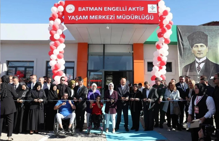 Görselin üst bölümünde, yeni bir merkezin açılış töreninde kurdele kesmek üzere yan yana dizilmiş protokol üyeleri, davetliler ve engelli bireyler yer alıyor. Giriş kapısının üzerinde kırmızı tabela zemininde beyaz harflerle "T.C. BATMAN ENGELLİ AKTİF YAŞAM MERKEZİ MÜDÜRLÜĞÜ" yazısı ve bakanlık logoları bulunuyor; kapının iki yanı kırmızı ve beyaz balonlardan yapılmış kemer sütunlarla süslenmiş durumda. Binanın sağ dış cephesinde ise kalpaklı dev bir Mustafa Kemal Atatürk posteri asılı duruyor. Ön planda, mavi tişörtlü tekerlekli sandalyeli bir erkek ile kırmızı tişörtlü tekerlekli sandalyeli bir genç kadın, yanlarındaki takım elbiseli protokol üyeleriyle birlikte ellerindeki makaslarla açılış kurdelesini kesiyor.