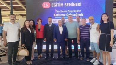 Kapalı bir alanda, büyük bir dijital ekranın önünde yan yana duran on kişilik bir grup görülüyor. Ekranda bir eğitim seminerine ait başlık ve tarih bilgileri yer alıyor. Grup, hatıra fotoğrafı çeker gibi kameraya doğru bakıyor. Kimi daha resmi, kimi daha günlük kıyafetler giymiş. Ortam düzenli, aydınlık ve bir etkinlik alanı havasında.