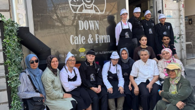 Görselde, Down Cafe & Fırın adlı işletmenin önünde bir grup insan toplu halde poz veriyor. Önlük ve aşçı boneleri giyen bazı çalışanlar arasında Down sendromlu bireyler de yer alıyor.