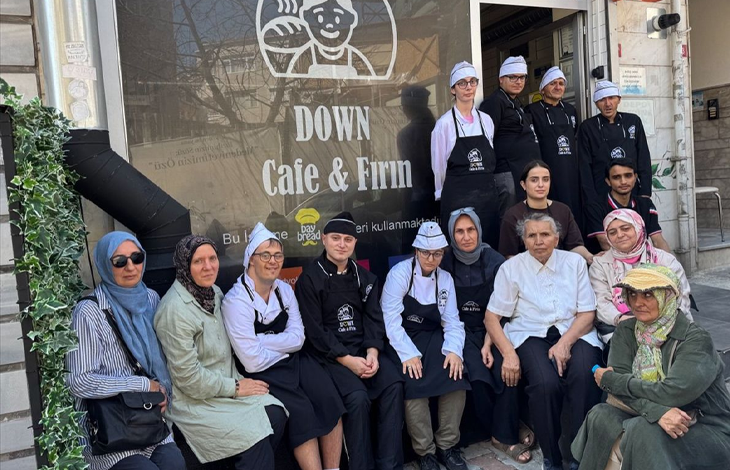 Görselde, Down Cafe & Fırın adlı işletmenin önünde bir grup insan toplu halde poz veriyor. Önlük ve aşçı boneleri giyen bazı çalışanlar arasında Down sendromlu bireyler de yer alıyor.