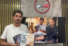 Görselde, beyaz tişörtlü bir erkek elinde dört kitap tutarak kameraya bakıyor. Arkasındaki ekranda aynı kişinin, yatakta oturan başka bir erkekle birlikte kitapları gösterdiği bir fotoğraf yer alıyor. Arka duvarda Nusaybin Kışla TV logosu görülüyor.