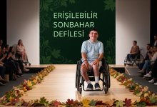 Sonbahar temalı bir moda podyumunda, tekerlekli sandalyede oturan bir model gülümseyerek izleyicilere bakıyor. Podyum kenarları dökülmüş yapraklarla süslenmiş. Arka planda “Erişilebilir Sonbahar Defilesi” yazısı yer alıyor. İzleyiciler arasında farklı erişilebilirlik ihtiyaçlarına sahip kişiler bulunuyor.