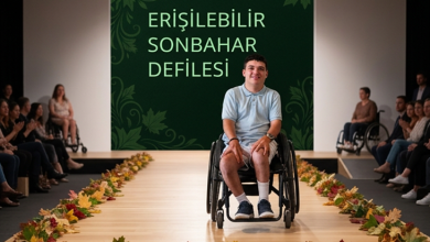 Sonbahar temalı bir moda podyumunda, tekerlekli sandalyede oturan bir model gülümseyerek izleyicilere bakıyor. Podyum kenarları dökülmüş yapraklarla süslenmiş. Arka planda “Erişilebilir Sonbahar Defilesi” yazısı yer alıyor. İzleyiciler arasında farklı erişilebilirlik ihtiyaçlarına sahip kişiler bulunuyor.