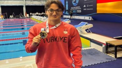 Para Yüzücü Turgut Aslan Yaraman, mercan renkli uzun kollu, Türkiye yazılı tişörtle ve boynunda bulunan madalyayla poz veriyor.