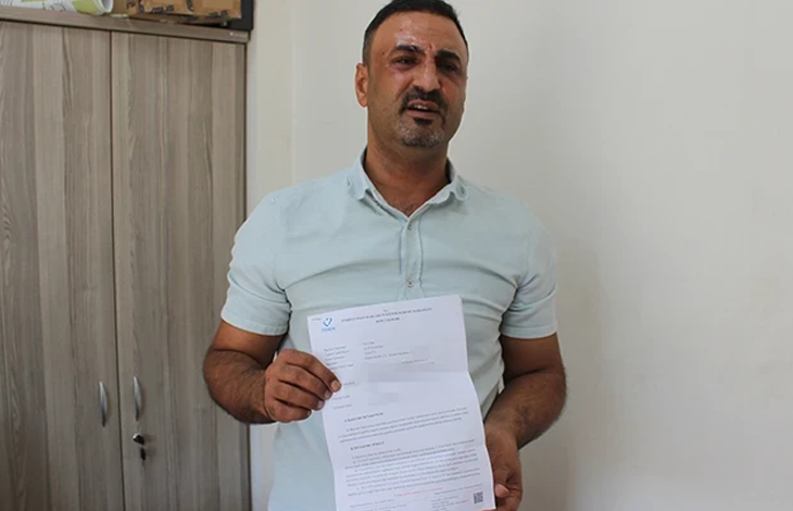 Görselin üst bölümünde, sade bir oda ortamında ayakta durarak elindeki resmî evrakı kameraya doğru gösteren orta yaşlı bir adam yer alıyor. Kısa koyu renkli saçlı, hafif sakallı ve açık yeşil/mint tonlarında kısa kollu polo yaka tişört giymiş olan adam, yüzünde üzüntülü ve mağdur bir ifadeyle doğrudan objektife bakıyor. İki eliyle öne doğru tuttuğu A4 boyutundaki resmî belgenin sol üst köşesinde mavi renkli bir kurum logosu ve altında maddeler hâlinde yazılmış resmî metinler ile barkod detayı görülüyor; arka planda ise ahşap bir ofis dolabı ve beyaz duvar seçiliyor.