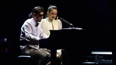 Görselin üst bölümünde, karanlık bir konser sahnesinde piyano başında yan yana performans sergileyen şarkıcı Karsu ile görme engelli müzisyen Şükrü Can Çapar yer alıyor. Sol tarafta piyano taburesinde oturan Çapar, siyah güneş gözlüğü, beyaz gömlek, siyah papyon ve kumaş pantolonuyla piyanonun tuşlarına basarak enstrümanı çalıyor. Sağ tarafında oturan Karsu ise sarı çiçek detaylı küpesi ve zarif beyaz sahne elbisesiyle piyanoya doğru eğilerek tebessümle mikrofon başında şarkı söylüyor; arka planda karanlık sahne atmosferi ve piyanonun yanında duran su şişesi ile nota sehpası görülüyor