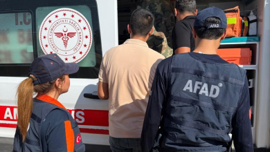 Görselin üst bölümünde, beyaz renkli bir ambulansın açık arka kapısı önünde toplanmış arama kurtarma personeli, sağlık görevlileri ve bulunan genç adam yer alıyor. Ön planda sırtında büyük beyaz harflerle "AFAD" yazılı lacivert yelek giymiş ve lacivert AFAD şapkası takmış bir görevli ile sol tarafında at kuyruklu saçları olan kadın bir sağlık/kurtarma personeli duruyor. Ortada ise bej renkli kısa kollu polo tişört giymiş genç adam, sağlık kontrolü ve ilk müdahale için ambulansa doğru yönlendirilirken görülüyor; arka planda ambulansın iç donanımı ve araç üzerindeki kırmızı-beyaz T.C. Sağlık Bakanlığı amblemi dikkat çekiyor.