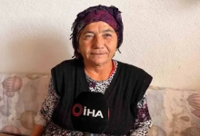 Görselde, mor bir başörtüsü takan Keziban Çiçeklioğlu desenli bir koltukta oturuyor. Üzerinde koyu renk bir yelek ve desenli bir bluz bulunuyor. Önünde, röportaj yapıldığını gösteren İHA logolu bir mikrofon yer alıyor. Arka planda açık renk bir duvar görülüyor. Kişi, sakin ve içten bir ifadeyle kameraya doğru konuşuyor gibi görünüyor.
