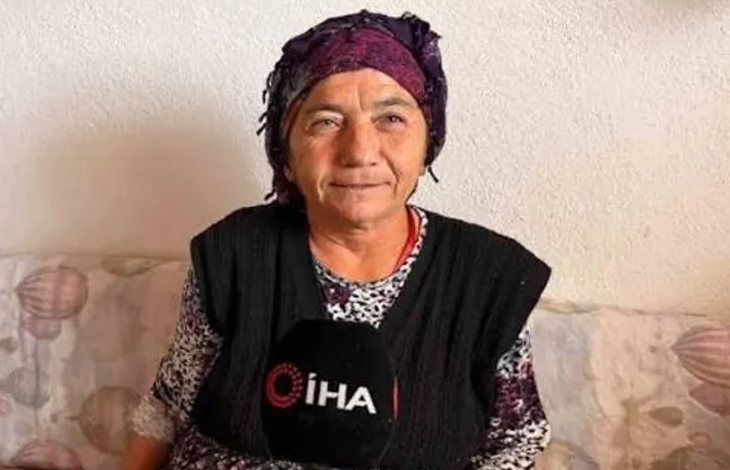 Görselde, mor bir başörtüsü takan Keziban Çiçeklioğlu desenli bir koltukta oturuyor. Üzerinde koyu renk bir yelek ve desenli bir bluz bulunuyor. Önünde, röportaj yapıldığını gösteren İHA logolu bir mikrofon yer alıyor. Arka planda açık renk bir duvar görülüyor. Kişi, sakin ve içten bir ifadeyle kameraya doğru konuşuyor gibi görünüyor.