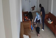 Görselin üst bölümünde, bir rehabilitasyon merkezinin bekleme veya dinlenme odasını yukarıdan gören güvenlik kamerası görüntüsü yer alıyor. Kahverengi deri koltukların bulunduğu odanın zemininde sırtüstü hareketsiz yatan bir birey, başında diz çökmüş mavi başörtülü bir kadın görevli ve ayakta duran personeller görülüyor. Arka plandaki beyaz kapının üzerinde büyük bir delik ve kırık hasarı dikkat çekerken, görevlilerin yerde yatan bireye müdahale ettiği anlar yansıyor.