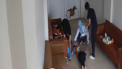 Görselin üst bölümünde, bir rehabilitasyon merkezinin bekleme veya dinlenme odasını yukarıdan gören güvenlik kamerası görüntüsü yer alıyor. Kahverengi deri koltukların bulunduğu odanın zemininde sırtüstü hareketsiz yatan bir birey, başında diz çökmüş mavi başörtülü bir kadın görevli ve ayakta duran personeller görülüyor. Arka plandaki beyaz kapının üzerinde büyük bir delik ve kırık hasarı dikkat çekerken, görevlilerin yerde yatan bireye müdahale ettiği anlar yansıyor.