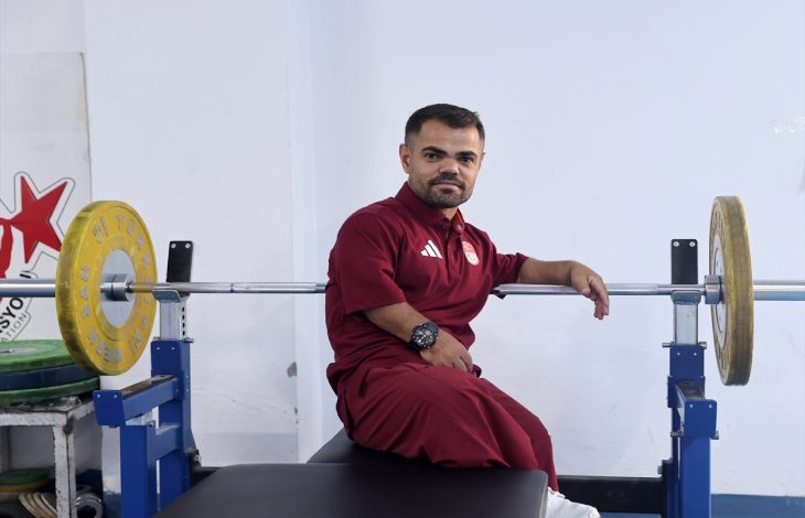 Görselde, spor salonunda ağırlık kaldırma ekipmanlarının yanında oturan, bordo renkli spor kıyafetleri giyen Abdullah Kayapınar bulunuyor.