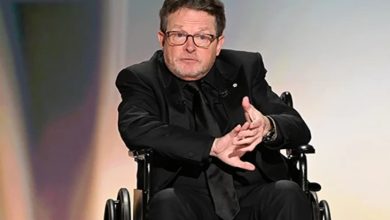 Michael J. Fox, tekerlekli sandalyede bulunuyor ve siyah takım elbiseli olarak konuşma yapıyor.