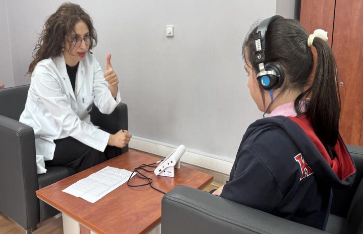 Görselde, klinik veya muayenehane ortamında bir uzman ile çocuk arasında gerçekleştirilen bir işitme testi seansı yer alıyor.