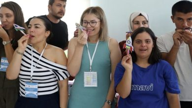 Bir grup kişi iç mekânda yan yana duruyor. Her biri elinde küçük bir kâğıt roket tutuyor ve roketi üfleyerek fırlatmaya hazırlanır gibi ağızlarına doğru götürmüş durumda. Üzerlerinde yaka kartları olan katılımcılar, etkinlik havasında neşeli ve dikkatli bir şekilde aynı hareketi yaparken görülüyor. Ortam aydınlık, samimi ve bir atölye ya da eğitim çalışması atmosferi taşıyor.