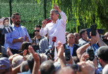 Özgür Özel, açık alanda kalabalığa hitap ederken görülüyor. Bir kürsü veya mikrofon önünde konuşma yapıyor; etrafında partililer ve vatandaşlar bulunuyor. Özel, el hareketleri ve yüz ifadesiyle vurgulu bir konuşma yaptığı izlenimi veriyor. Arkada parti bayrakları veya etkinlik alanına ait görseller yer alıyor.