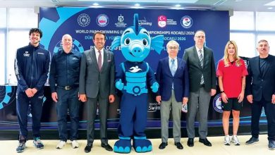 Yedi kişi, “World Para Swimming European Championships Kocaeli 2026” yazılı tanıtım panosu önünde poz veriyor. Ortada mavi, sevimli bir su canlısı maskotu duruyor. Ortam resmi bir tanıtım etkinliği havasında.