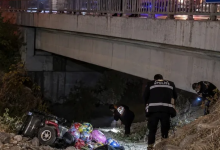 Görselin üst bölümünde, gece saatlerinde bir köprünün veya viyadüğün altındaki dere yatağında gerçekleşen kaza yeri incelemesi yer alıyor. Sol alt tarafta, şarampole devrilmiş kırmızı gövdeli akülü sandalye ve hemen yanında etrafa saçılmış rengarenk uçan balonlar görülüyor. Sağ tarafta ve arka planda ise sırtlarında beyaz harflerle "POLİS" yazılı üniformalı polis memurları, fener ışığı eşliğinde dere yatağında ve köprü altında inceleme yapıyor. Üst kısımda ise korkulukları ve beton kirişleri seçilen köprü yer alıyor.
