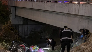 Görselin üst bölümünde, gece saatlerinde bir köprünün veya viyadüğün altındaki dere yatağında gerçekleşen kaza yeri incelemesi yer alıyor. Sol alt tarafta, şarampole devrilmiş kırmızı gövdeli akülü sandalye ve hemen yanında etrafa saçılmış rengarenk uçan balonlar görülüyor. Sağ tarafta ve arka planda ise sırtlarında beyaz harflerle "POLİS" yazılı üniformalı polis memurları, fener ışığı eşliğinde dere yatağında ve köprü altında inceleme yapıyor. Üst kısımda ise korkulukları ve beton kirişleri seçilen köprü yer alıyor.