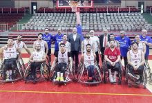 Tekerlekli Sandalye Basketbol A Millî Erkek Takımı, bir spor salonunda toplu hâlde poz veriyor. Ön sırada millî formalarını giymiş sporcular tekerlekli sandalyelerinde oturuyor; arkalarında ise teknik ekip ve destek kadrosu ayakta duruyor. Arka planda pota ve tribünler görülüyor. Takımın duruşu güçlü, disiplinli ve birlik duygusunu yansıtan bir millî takım atmosferi oluşturuyor.