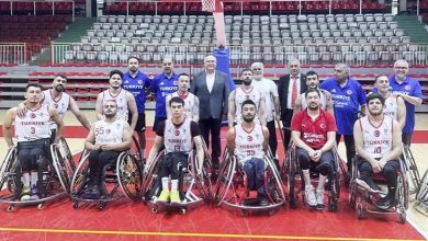 Tekerlekli Sandalye Basketbol A Millî Erkek Takımı, bir spor salonunda toplu hâlde poz veriyor. Ön sırada millî formalarını giymiş sporcular tekerlekli sandalyelerinde oturuyor; arkalarında ise teknik ekip ve destek kadrosu ayakta duruyor. Arka planda pota ve tribünler görülüyor. Takımın duruşu güçlü, disiplinli ve birlik duygusunu yansıtan bir millî takım atmosferi oluşturuyor.