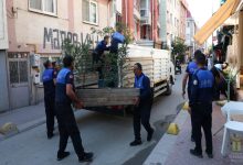 Görselde, dar bir sokakta belediye zabıta ekiplerinin bir kamyonete yükledikleri uzun ahşap masayı taşırken ve çevredeki eşyaları düzenlerken görülüyor.