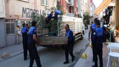 Görselde, dar bir sokakta belediye zabıta ekiplerinin bir kamyonete yükledikleri uzun ahşap masayı taşırken ve çevredeki eşyaları düzenlerken görülüyor.