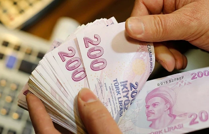 Görselin üst bölümünde, bir kişinin elleri arasında tuttuğu ve saydığı deste hâlindeki pembe renkli 200 Türk Lirası banknotlar yer alıyor. Ön plandaki banknotun üzerinde Yunus Emre portresi ve "200 İKİ YÜZ TÜRK LİRASI" ibaresi net bir şekilde görülürken, kişinin parmakları desteyi hafifçe aralamış vaziyette duruyor; sol arka planda ise ofis ortamını çağrıştıran hesap makinesi veya klavye tuşları flu olarak seçiliyor.