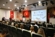 Adana 1. Otizm Zirvesinde, izleyici koltuklarında oturan katılımcılar kürsüde konuşma yapan kişiyi dinliyor.
