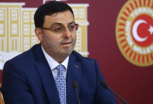AK Parti İstanbul Milletvekili Serkan Bayram, TBMM’de düzenlenen bir basın açıklaması sırasında kürsüde konuşuyor. Üzerinde koyu renk takım elbise, beyaz gömlek ve desenli mavi bir kravat bulunuyor. Arka planda Türkiye Büyük Millet Meclisi amblemleri ve Türk bayrağı yer alıyor.
